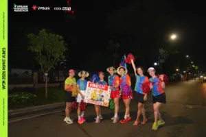 Nhóm chị em đội nón lá, cầm pom-pom nhiều màu và biển FINISH tạo dáng giữa đường chạy trong đêm