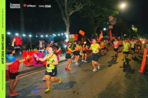 Runner chạy qua trạm cổ vũ dưới dây đèn, các thành viên đội cổ vũ giơ pom-pom và chìa tay chào