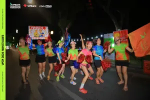 Đội cổ vũ nhảy múa cầm pom-pom đỏ, xanh và cờ cam trên đường lúc đêm, ánh sáng kéo thành vệt