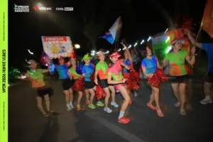 Hàng cổ vũ nhún nhảy hò reo với pom-pom đỏ và biển FINISH, ánh đèn lướt thành vệt sáng trong đêm